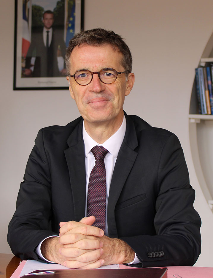 Portrait de Philippe Dulbecco, assis à son bureau, en tenue formelle, dans un cadre professionnel – photo officielle.
