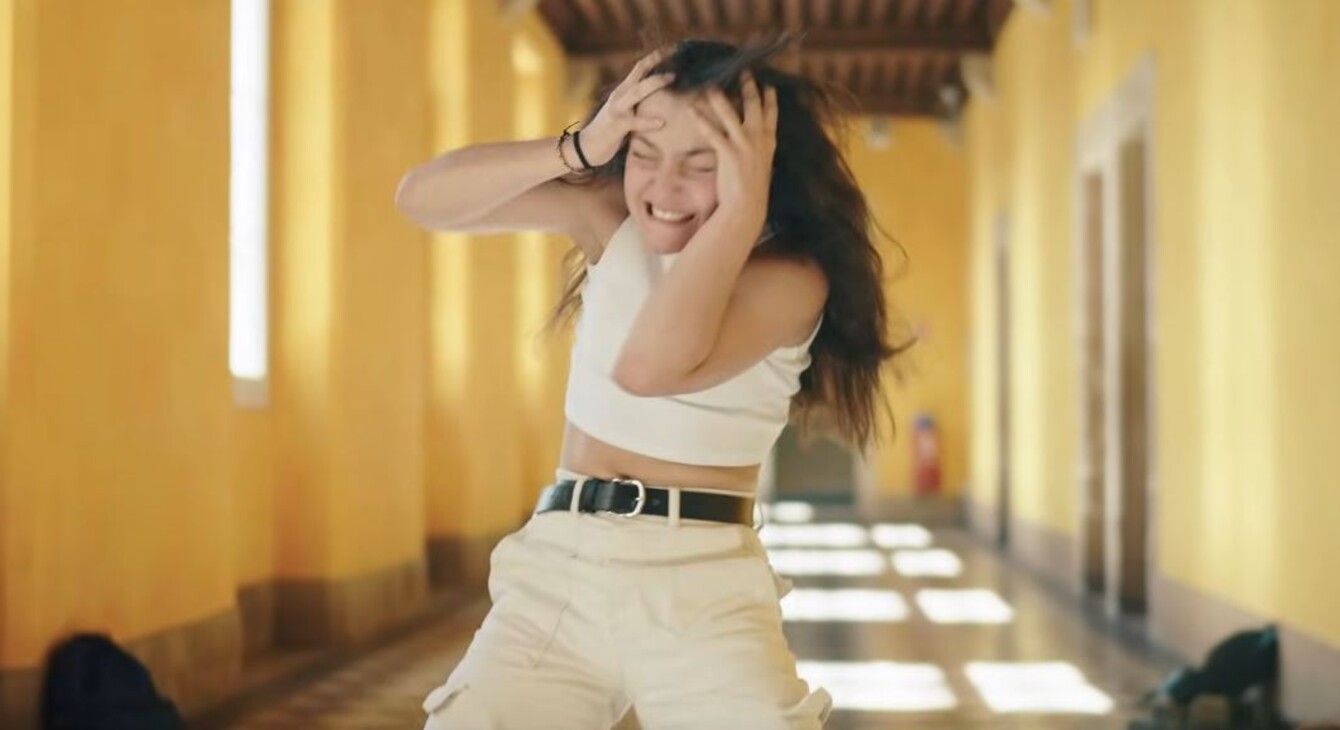 Capture du clip vidéo dans lequel une élève se tient la tête dans les mains dans un grand couloir vide