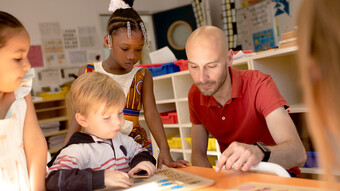 Un enseignant est assis dans une salle de classe et montre un document à 4 élèves.